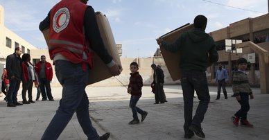 Syrian Arab Red Crescent volunteers move boxes with winter clothes for children to a schoolyard where approximately 30 displaced families live. Photo: KRZYSIEK, Pawel/ICRC