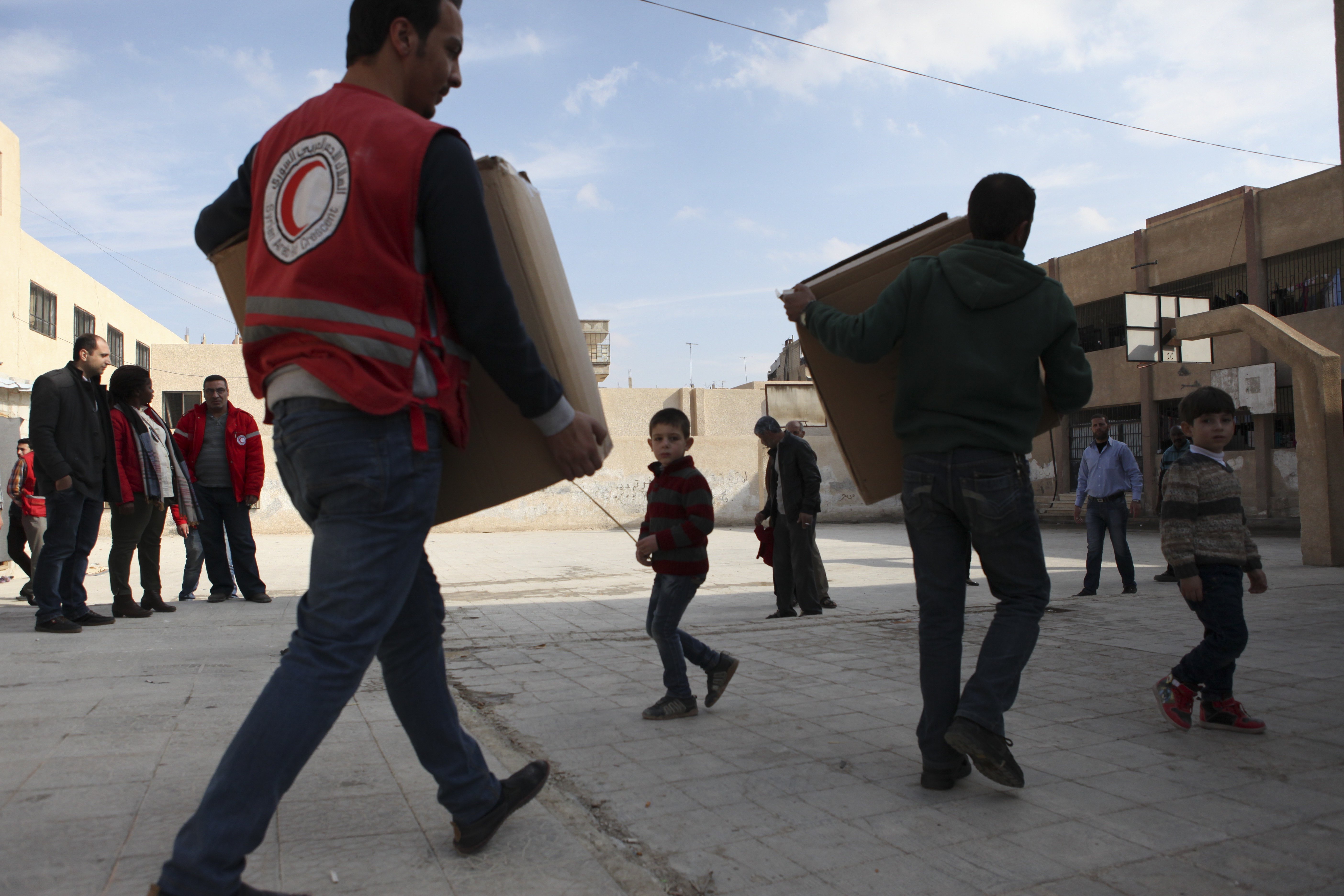 Syrian Arab Red Crescent volunteers move boxes with winter clothes for children to a schoolyard where approximately 30 displaced families live. Photo: KRZYSIEK, Pawel/ICRC