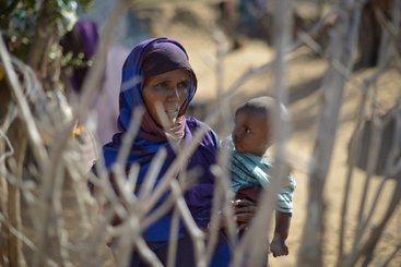 A mother and her child stand next to their home behind a fence at an IDP settlement next to the village of Ambresso, Somalia, on August 22, 2016