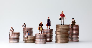Miniature people standing on piles of different heights of coins